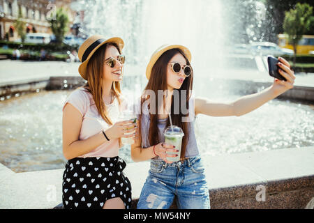 Glückliche junge Frauen, die zwei Freunde von selfie Smartphone und trinken Cocktails getränke Outdoor im Sommer Straße Stockfoto