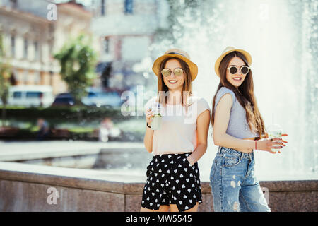 Zwei junge Frauen trinken bunte Cocktails aus Flaschen auf der Straße. Stockfoto