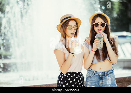 Zwei junge Frauen trinken bunte Cocktails aus Flaschen auf der Straße. Stockfoto