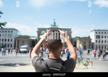 Nahaufnahme eines jungen kaukasischen Mann, von hinten gesehen, ein Bild von der beliebten Brandenburger Tor in Berlin, Deutschland, mit seinem Smartphone Stockfoto