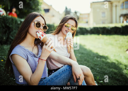 Porträt von zwei jungen Frauen sitzen auf einem Bordstein essen Eis in der Waffel Horn im Sommer Straße Stockfoto