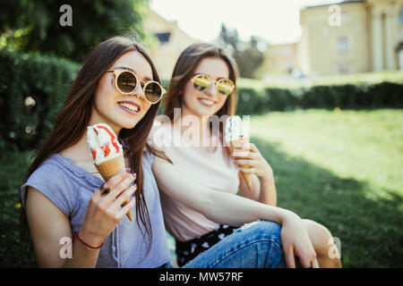 Porträt von zwei jungen Frauen sitzen auf einem Bordstein essen Eis in der Waffel Horn im Sommer Straße Stockfoto