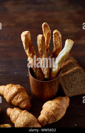 Blätterteiggebäcke auf dunklen Holztisch, Nahaufnahme, selektiver Fokus, Hintergrundbeleuchtung. Leckere frisch gebackene Grissini und hausgemachte croissats auf rustikalen backgro Stockfoto