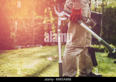 Der Mann hält Gartengeräte. Der Gärtner hat eine Gartenschere, eine Schaufel, Schere und andere Tools mit ihm. Arbeiten im Garten, Pflege für den Garten. Stockfoto