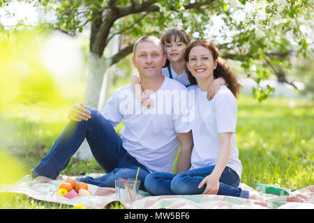 Eltern und ein 5 Jahre alten Tochter Sitzen im Garten unter einem blühenden Apfelbaum. Stockfoto