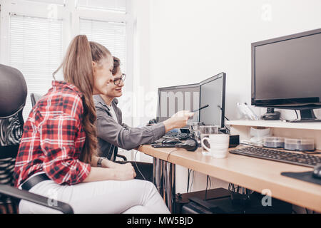 Bild der glücklichen jungen Kolleginnen und Kollegen im Büro coworking mithilfe von Desktop Computern und diskutieren neue Idee. Stockfoto