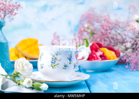 Eine Tasse duftenden Kaffee, Obst und Eis und Blüten sind weiss und rosa auf einem blauen Hintergrund aus Holz. Vintage Foto. Platz kopieren Stockfoto