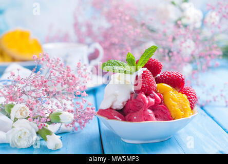 Eis von hellen Blüten mit Himbeeren und Minze in einer Platte, auf blauem Holz- Hintergrund. Eine Tasse Kaffee am Morgen und Licht und Blumen. Vintage Foto. Platz kopieren Stockfoto