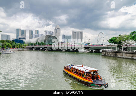 Eine Kreuzfahrt Boot wie die twakows Fahrt durch die berühmten Singapore River bekannt. Das Gebäude an der Rückseite ist die berüchtigte Theater an der Bucht, Esplanade. Stockfoto