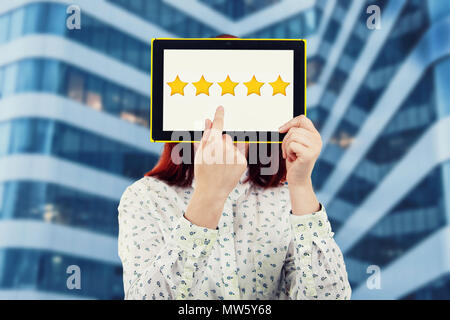 Junge Geschäftsfrau, die ihr Gesicht mit einem digitalen Tablet mit fünf goldene Sterne auf dem Bildschirm versuchen, ein Feedback zu wählen. Exzellenter Kundenservice serv Stockfoto