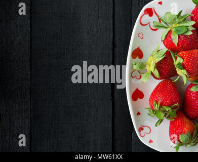 Die Hälfte der Erdbeeren, die auf schwarzen Holztisch Stockfoto