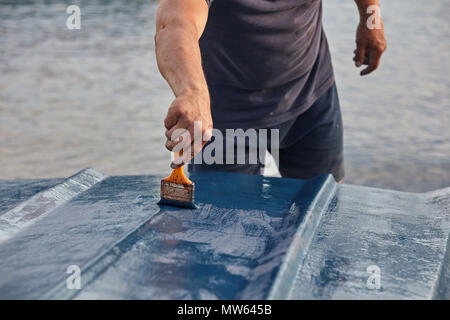 Mann Malerei Boot. Detailansicht von Hand mit einem Pinsel mit blauer Farbe. Stockfoto