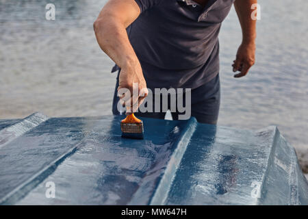 Mann Malerei Boot. Detailansicht von Hand mit einem Pinsel mit blauer Farbe. Stockfoto