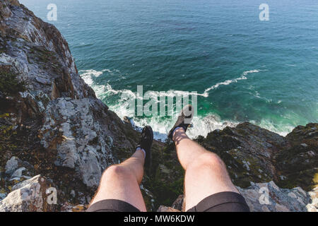 Mann sitzt am Rand der Klippe über Ozean am Cape Point in Kapstadt Stockfoto