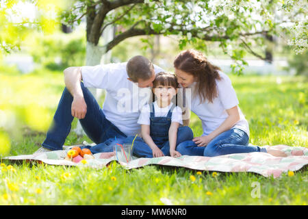 Eltern und ein 5 Jahre alten Tochter Sitzen im Garten unter einem blühenden Apfelbaum. Stockfoto