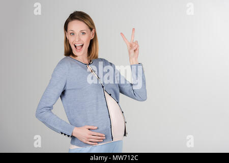 Porträt der glückliche junge schwangere Frau posiert im Studio isoliert auf Grau Stockfoto