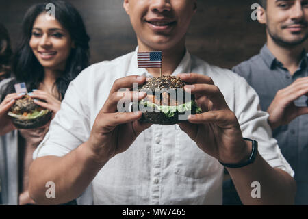 7/8 Schuß von lächelnden jungen Menschen Hamburger Holding mit kleinen amerikanischen Flaggen Stockfoto