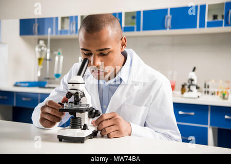 Junge Techniker in Uniform mit einem Mikroskop im Labor Umgebung Stockfoto