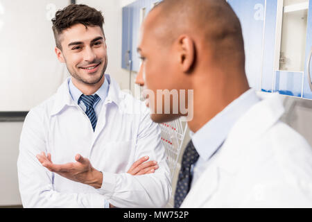 Zwei junge Ärzte in Laborkitteln lächelnd und Diskussion über die Arbeit im Labor Stockfoto