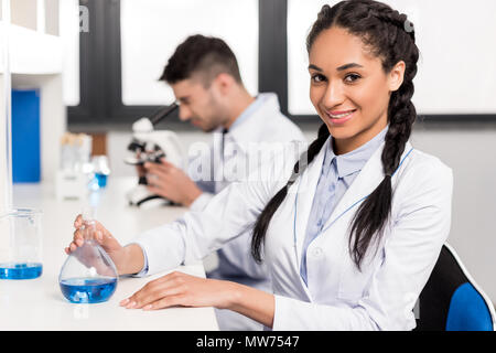 Junge Wissenschaftler in laborkittel am Tisch im Labor mit Reagenzglas saßen und an Kamera Stockfoto
