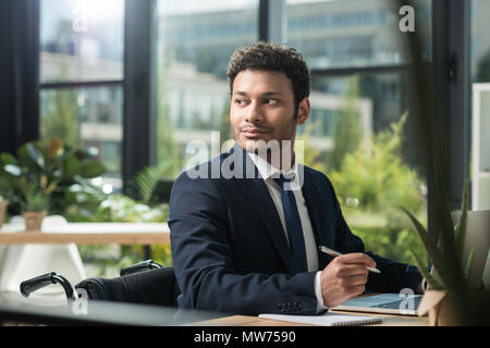 Portrait von Behinderten afrikanische amerikanische Geschäftsmann weg schauen, während am Arbeitsplatz sitzt mit Laptop im Büro Stockfoto