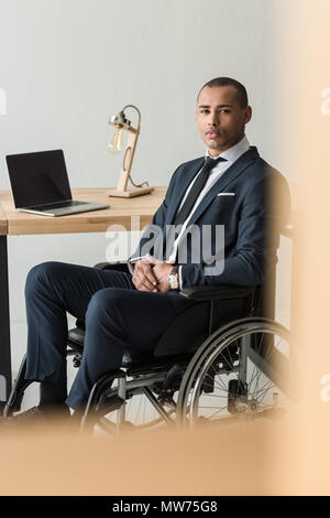 Afrikanische amerikanische Geschäftsmann auf Kamera, während am Arbeitsplatz sitzt mit Laptop im Büro deaktiviert Stockfoto