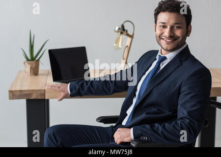 Afrikanische amerikanische Geschäftsmann auf Kamera, während am Arbeitsplatz sitzt mit Laptop im Büro deaktiviert Stockfoto