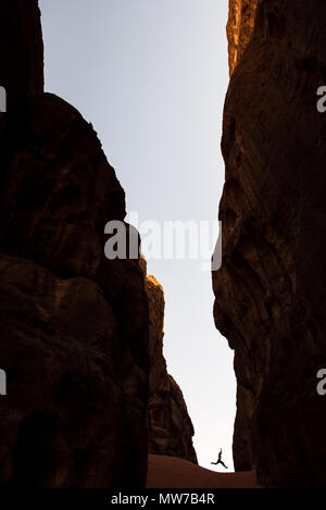 Mädchen springen in eine enge Schlucht. Silhouette einer tiefen Schlucht mit senkrechten Wänden. Wadi Rum, Jordanien Stockfoto