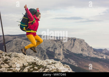Mädchen mit Rucksack auf einer Klippe springen, in den Bergen Stockfoto