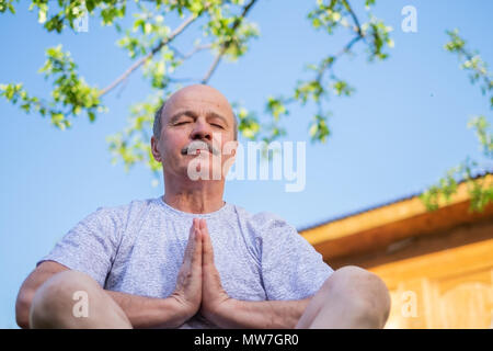 Friedliche ältere Menschen meditieren sitzt ooutdoor unter den Baum. Stockfoto