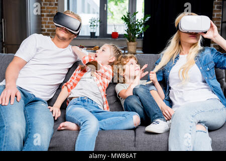 Adorable kleine Kinder auf Eltern mit Virtual reality Headsets zu Hause Stockfoto