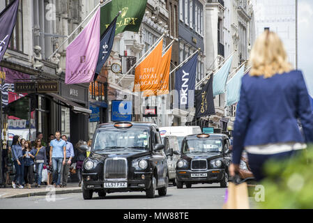 Ein anstrengender Tag im Einkaufsviertel von Mayfair. Frauen mit Einkaufstaschen gehen, während schwarze Taxis die Straße mit Markenfahnen herunterfahren Stockfoto