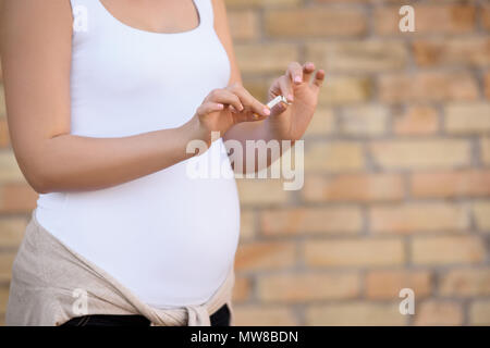 7/8-Ansicht der schwangeren Frau in weißen Kleidern Zigarette brechen Stockfoto