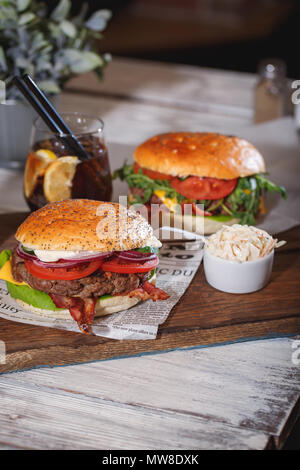 Zwei frische Classic Burger mit Rindfleisch, Käse, Speck, Zwiebel, Tomaten und Salat auf Holztisch. Stockfoto