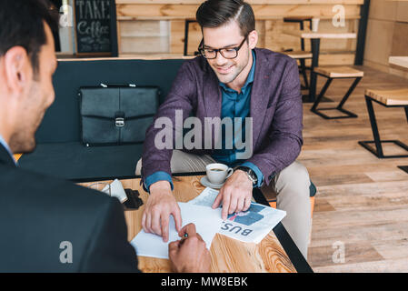 Lächelnd Geschäftsmann im Vertrag, dass Kollege Unterzeichnung während der Sitzung im Cafe zeigen Stockfoto