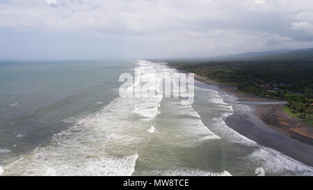 Tropical Beach bei bewölktem Wetter. Luftaufnahme von großen Wellen am Strand mit schwarzem Sand vulkanischen Ursprungs im windigen Wetter, Bali. Marine Meer, Himmel, Meer. Travel Concept. Stockfoto