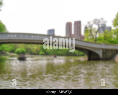 Defokussiertem Hintergrund des berühmten Bogen Brücke und Touristen auf Kanu im Hintergrund im Central Park, New York City, USA. Absichtlich verschwommene Postproduktion für bokeh Wirkung. Stockfoto