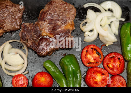 Rib Eye Steak (spanisch: Bife Ancho), Zwiebeln, Tomaten und Paprika auf rechteckigem Gusseisen flache Pfanne gegrillt, flach legen Stockfoto