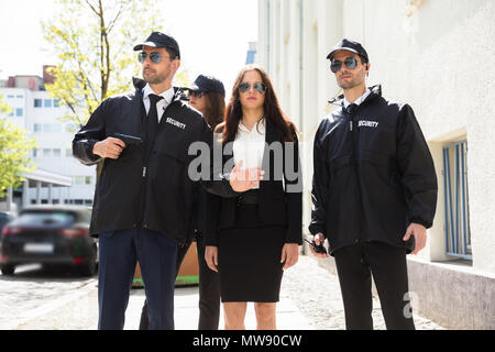 Portrait von schönen jungen Geschäftsfrau mit Bodyguards auf Bürgersteig Stockfoto