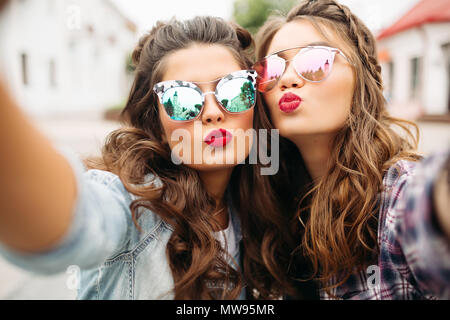 Wunderschöne brünette Freundinnen mit Frisur, verspiegelten Sonnenbrillen und roten Lippen, selfie mit Ente Gesicht. Stockfoto