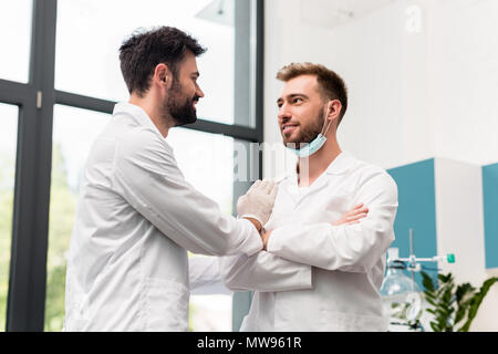 Zwei schöne junge männliche Wissenschaftler in weißen Kitteln reden und lächeln einander im chemischen Labor Stockfoto