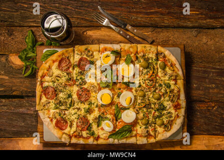 Aboive Aussicht auf leckere Pizza mit Salami, Mozzarella, Tomatensauce und gekochte Stücke von Eiern auf einem Holztisch, Frühstück Stockfoto