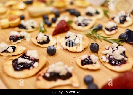 Lecker und appetitlich Feta Käse mit Schwarze Johannisbeere Cracker auf Anzeige auf Holz Schneidebrett mit Rosmarin, Heidelbeeren, Erdbeeren, USA Stockfoto