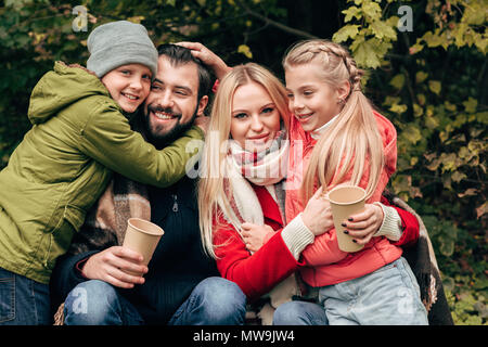 Glückliche junge Familie mit zwei Kindern umarmen und halten Pappbecher im Herbst Park Stockfoto