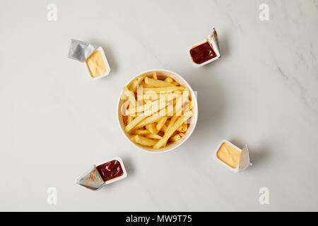 Blick von oben auf die leckere Pommes frites in der Schüssel mit Behältern von Saucen umgeben auf Weiß Stockfoto