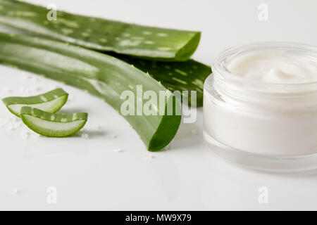 Detailansicht der organischen Creme in Container, Aloe Vera Blätter und Scheiben auf weiße Oberfläche mit Salz Stockfoto