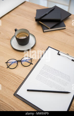 Nahaufnahme der Tasse Kaffee, Brillen, Dokumente auf hölzernen Tischplatte Stockfoto