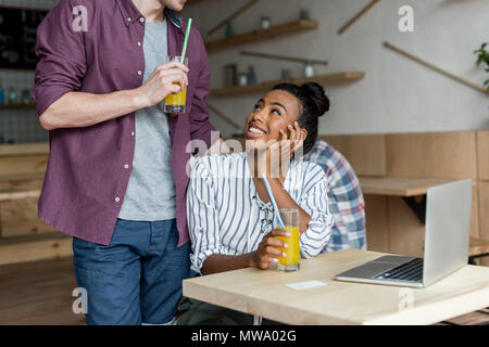 7/8 Schuß von jungen multiethnischen Paar Saft trinken und mit Laptop im Cafe Stockfoto