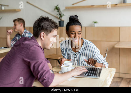 Glückliche junge Multiethnischen Paar mit Laptop beim Trinken Kaffee im Cafe Stockfoto