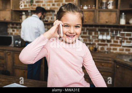 Glückliches Kind sprechen per Telefon Küche während Vater kochen Frühstück auf Hintergrund verschwommen Stockfoto